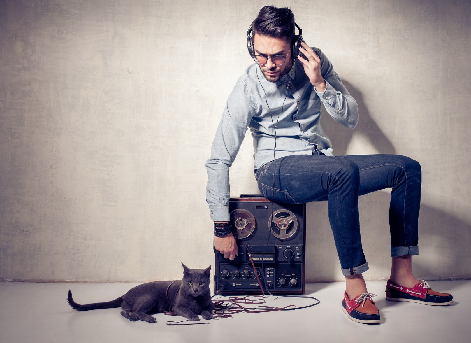 handsome man and cat listening to music on a magnetophone against grunge wall